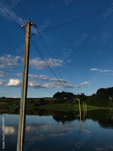 Tranquil rural landscape with telephone poles and cloudy sky reflection