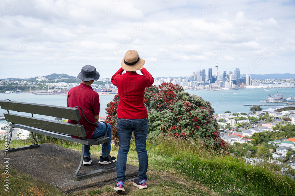 Couple enjoying the views of Auckland Sky Tower and skyline. Pohutukawa trees in full bloom. New Zealand Christmas tree.