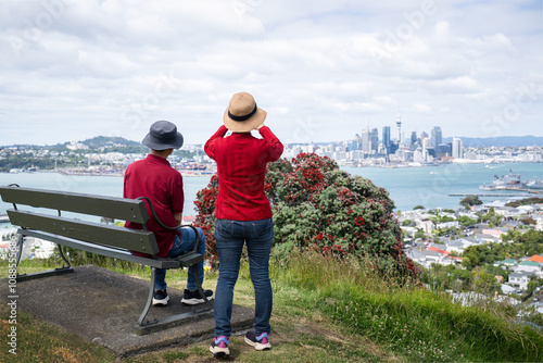 Obraz na płótnie Couple enjoying the views of Auckland Sky Tower and skyline. Pohutukawa trees in full bloom. New Zealand Christmas tree. w salonie