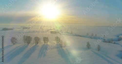 Drone aerial view of cold winter landscape arctic field, trees covered with frost snow, ice river and sun rays over horizon. Extreme low temperature weather.