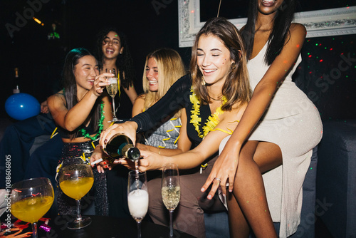 Canvas Print A lively group of young women enjoying a night out at a night club, sharing laughter and pouring champagne
