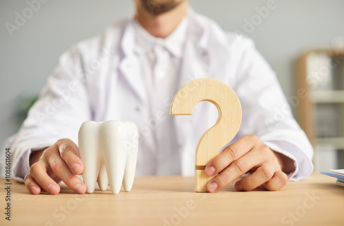 Professional dentist ready to answer all your questions about teeth health. Closeup male hands holding a white tooth model and a wooden question mark on the table. Dental care, stomatology concept