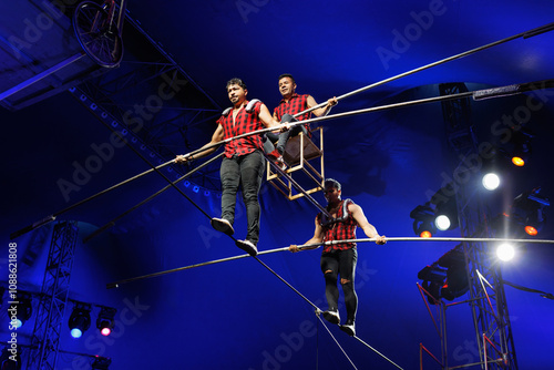 Aerial acrobats hold a rope with a chair on which a tightrope walker stands. A circus trick.