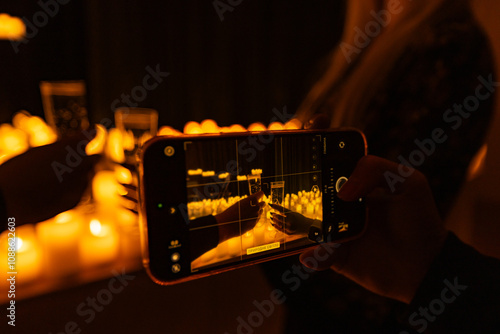 hands with phone taking video of symphonic orchestra on stage with lots of candles