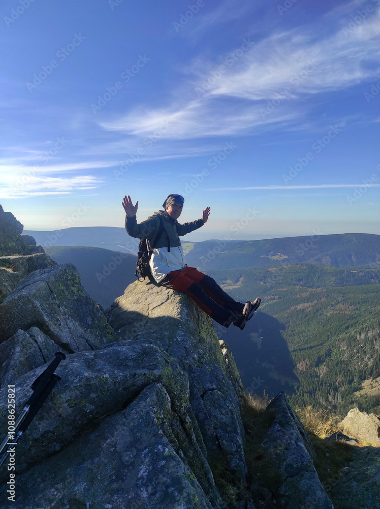 Male tourist with backpack sits on edge of cliff at Snezka mountain, Poland, Czech Republic Male tourist with backpack sits on edge of cliff at Snezka mountain, Poland, Czech Republic