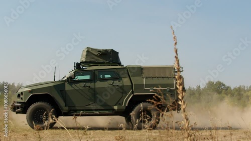 A military armored vehicle moves across a rural field, raising dust as it navigates the terrain. The scene highlights the operational readiness and mobility of military forces during the war in Ukrain