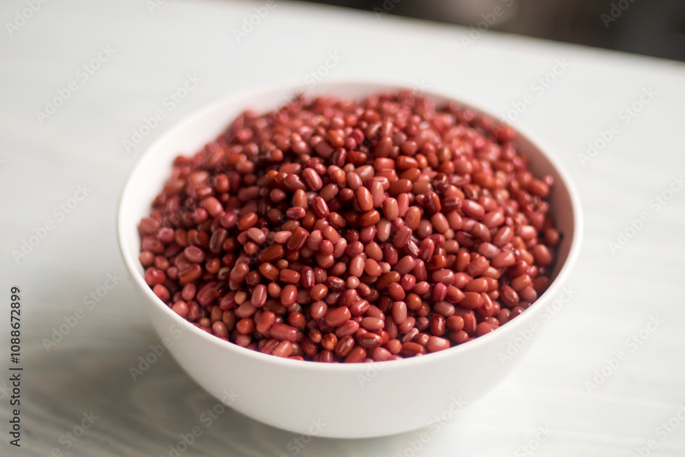 Azuki or Adzuki beans (Japanese red bean or red mung bean) after soaked in white bowl isolated on a table closed up. Selective focus blurred background. Azuki or Adzuki beans (Japanese red bean or red mung bean) after soaked in white bowl isolated on a table closed up. Selective focus blurred background.