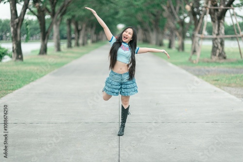 Happy young woman dancing joyfully on a sunny day in a scenic park setting, wearing casual clothing with a playful expression and beautiful nature backdrop. photo