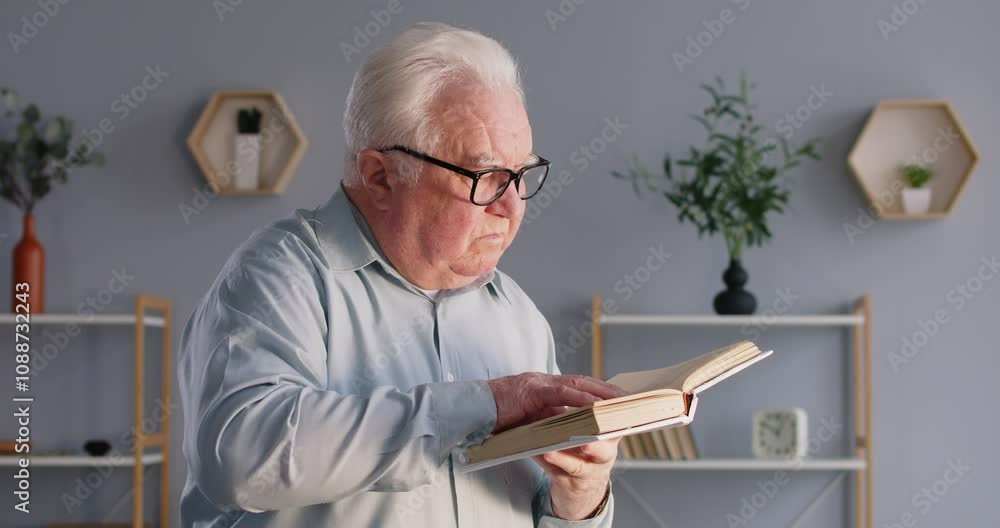 Concentrated and calm elderly man at home, enjoying domestic leisure time by reading a book or literature. Essence of relaxation from favorite hobby and the joy of reading at home library.