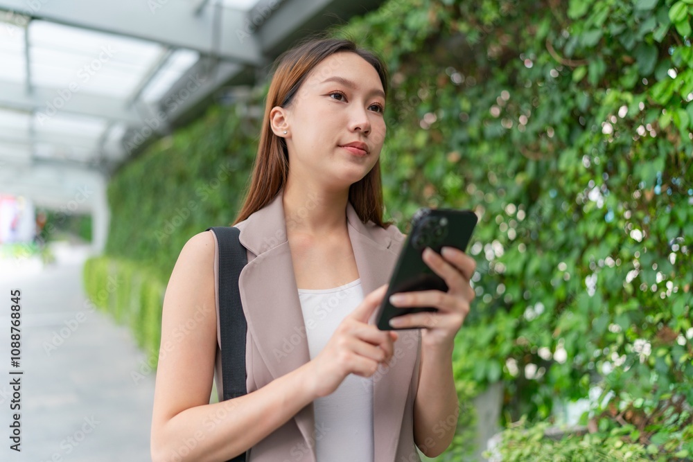 Asian Woman Using Phone While Walking Across a Greenery Background Asian Woman Using Phone While Walking Across a Greenery Background