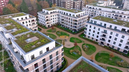 Drone video of modern residential buildings with green roofs and a lush courtyard in Berlin Reinickendorf. The scene highlights sustainable urban living and eco-friendly architecture. Drone move right