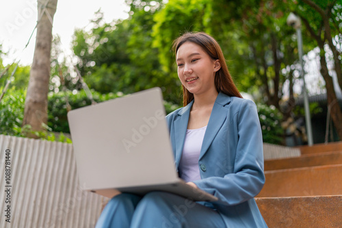 Asian Woman Sitting In A Garden and Using Laptop