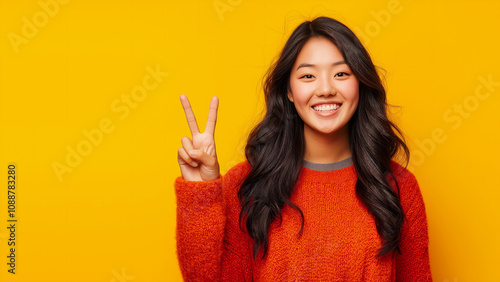 Asian woman smiling and making peace sign, copy space, single color background