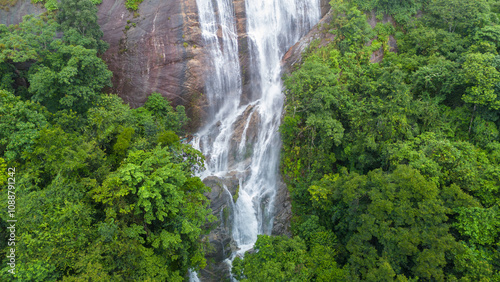 Aerial view of beautiful waterfall village in the lush green rain cloud and foggy cover tropical rain forest mountain during the rainy season. Beautiful landscape with high mountain