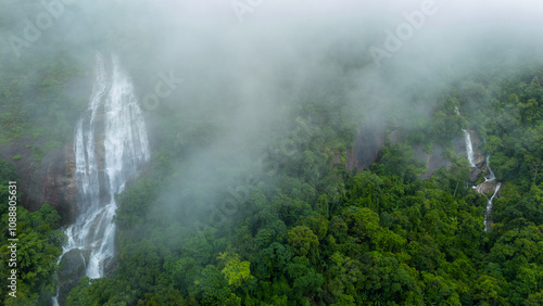 Aerial view of beautiful waterfall village in the lush green rain cloud and foggy cover tropical rain forest mountain during the rainy season. Beautiful landscape with high mountain photo