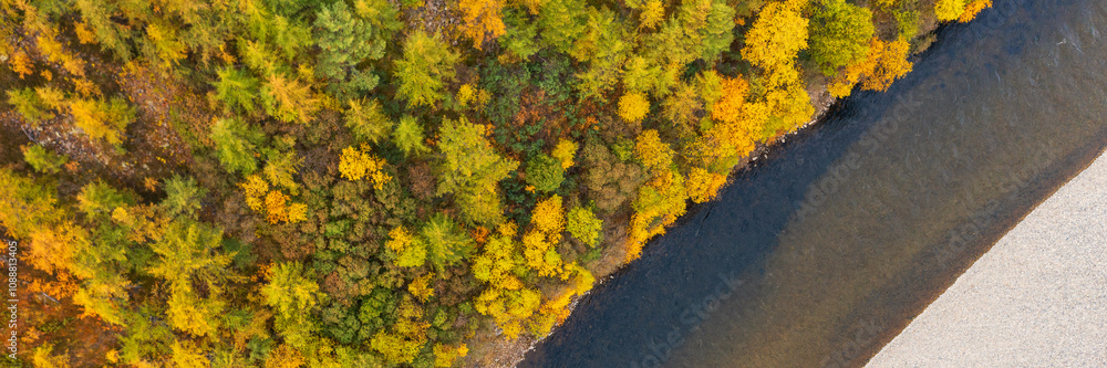 Panoramic autumn aerial photograph of the river. Top view of the river bed and the riverbank overgrown with larch forest. Colorful autumn trees with yellowed foliage. Fall season. Natural background. Panoramic autumn aerial photograph of the river. Top view of the river bed and the riverbank overgrown with larch forest. Colorful autumn trees with yellowed foliage. Fall season. Natural background.