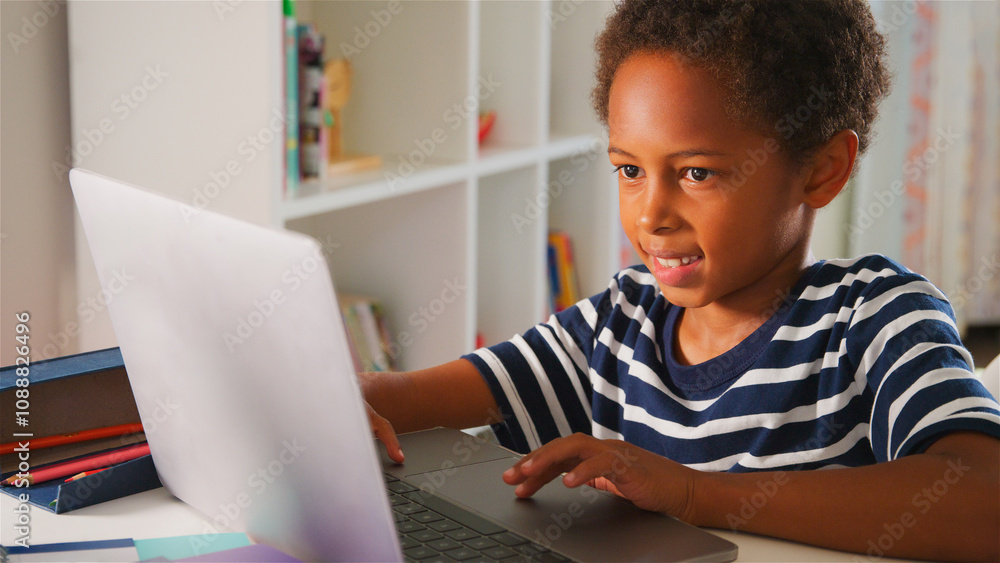 Young Boy Sitting At Desk In Bedroom At Home Using Laptop Computer Young Boy Sitting At Desk In Bedroom At Home Using Laptop Computer