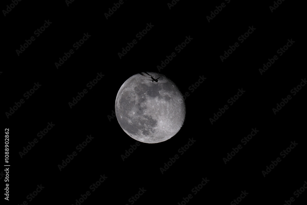The moon in the night sky with a silhouette of an airplane. The moon in the dark sky with a plane flying over it. The moon in the night sky with a silhouette of an airplane. The moon in the dark sky with a plane flying over it.