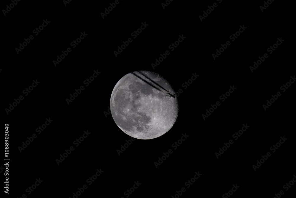 The moon in the night sky with a silhouette of an airplane. The moon in the dark sky with a plane flying over it. The moon in the night sky with a silhouette of an airplane. The moon in the dark sky with a plane flying over it.