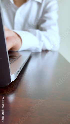 テーブルの上でノートパソコンをタイピングする若い女性・白いシャツ・縦長・ビデオ