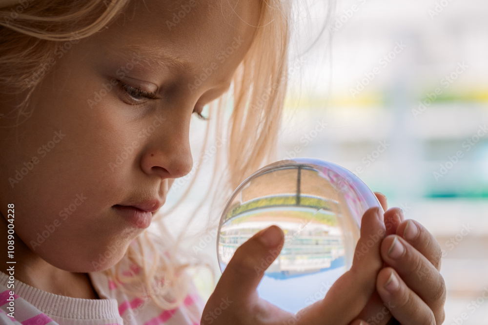 Young girl closely observing a glass crystal ball with reflections and a soft natural light Young girl closely observing a glass crystal ball with reflections and a soft natural light