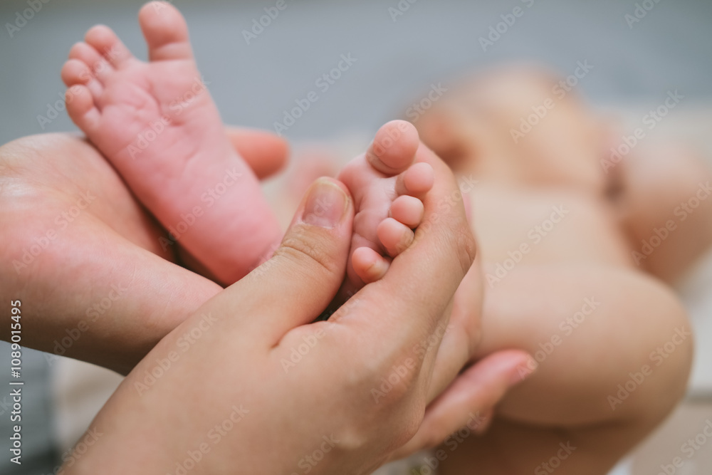 The palms of the mother are holding the foot of the newborn asian baby. Close-up family photo of a child's toes, heels and feet. The palms of the mother are holding the foot of the newborn asian baby. Close-up family photo of a child's toes, heels and feet.