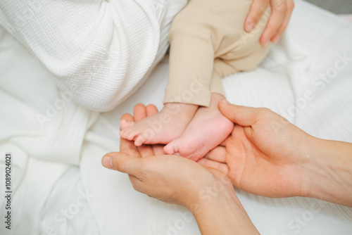 The palms of the mother are holding the foot of the newborn asian baby. Close-up family photo of a child's toes, heels and feet.