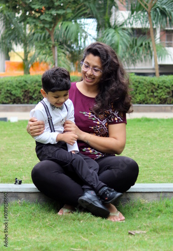 mummy is playing with her 3 year old son in the park. Boy wearing party wear and enjoying his bond with his bother. they are having fun and laughing out loud. Child is ready for fancy dress day.  photo