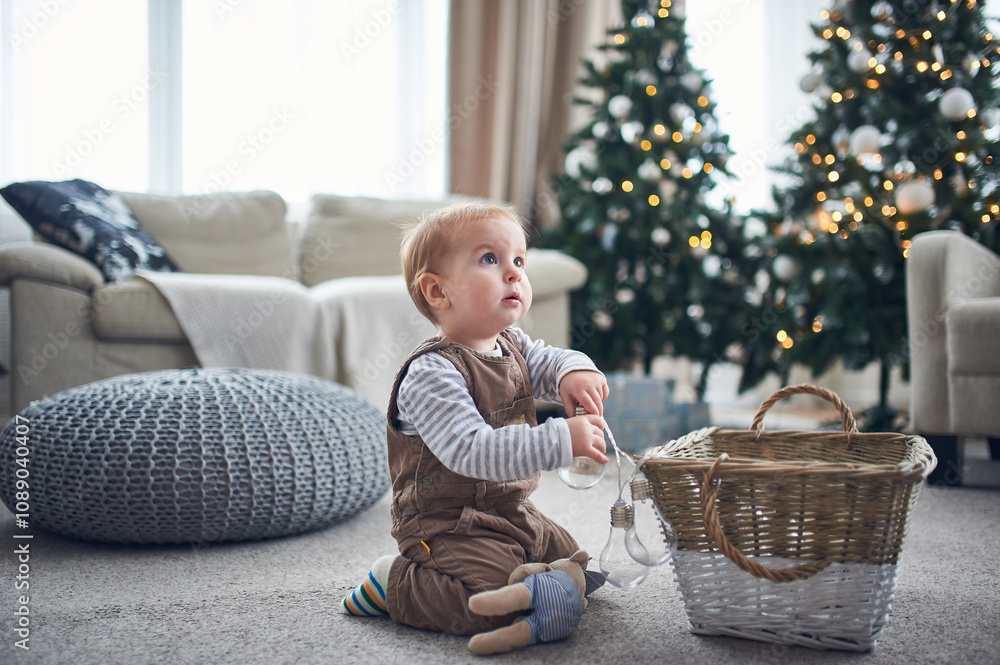 Naklejka premium Child playing with a basket of ornaments in a cozy living room decorated for the holidays