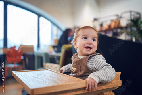 Happy baby enjoys time in a wooden high chair at a cozy indoor cafe photo