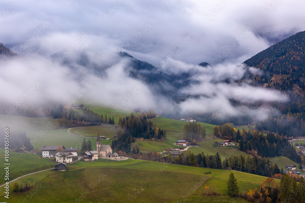 Fototapeta premium Autumn View of Santa Maddalena in the Dolomites Covered in Morning Fog with Colorful Fall Meadow and Scenic Mountain Background