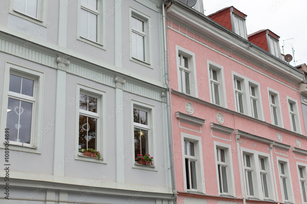 Obraz premium Two remarkable historical buildings in the city feature beautiful pastel facades, crafted windows, and vibrant flower boxes, adding unique charm and character to the urban landscape