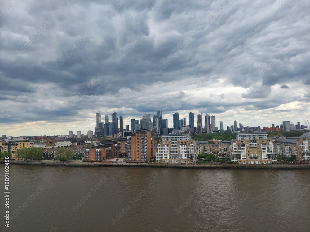 Obraz premium Cloudy Urban Skyline Over River in Modern Cityscape