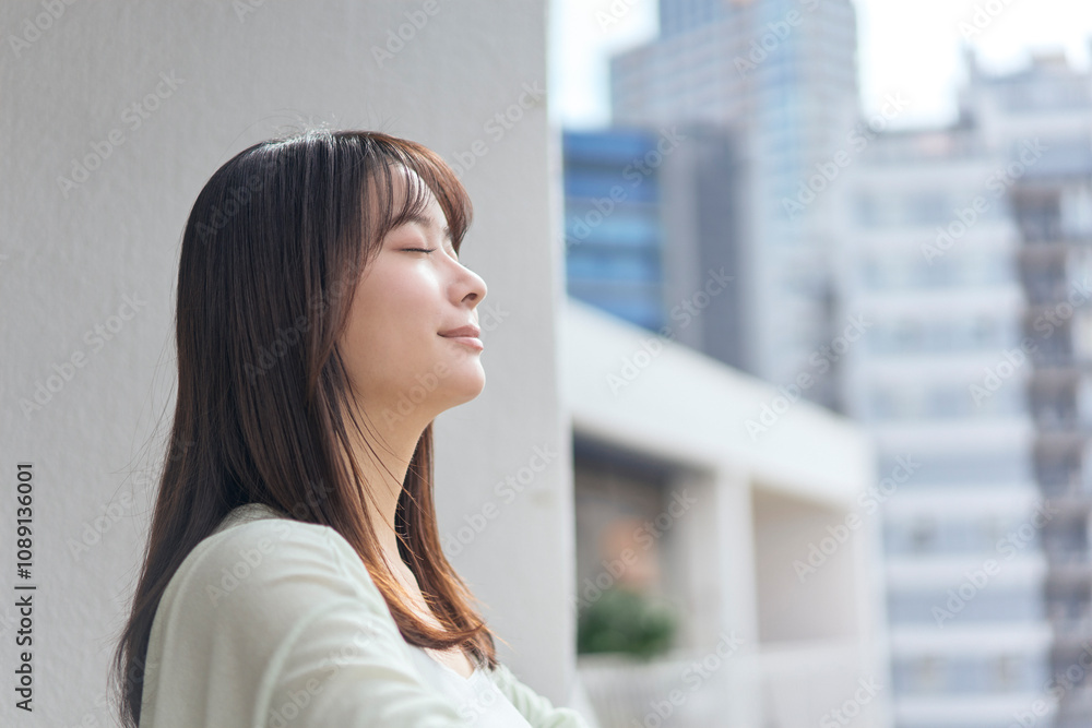 Fototapeta premium ベランダに出て深呼吸をする若い女性。