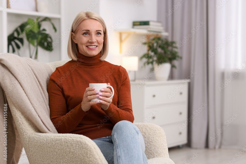 Smiling middle aged woman with cup of hot drink on armchair at home. Space for text Smiling middle aged woman with cup of hot drink on armchair at home. Space for text