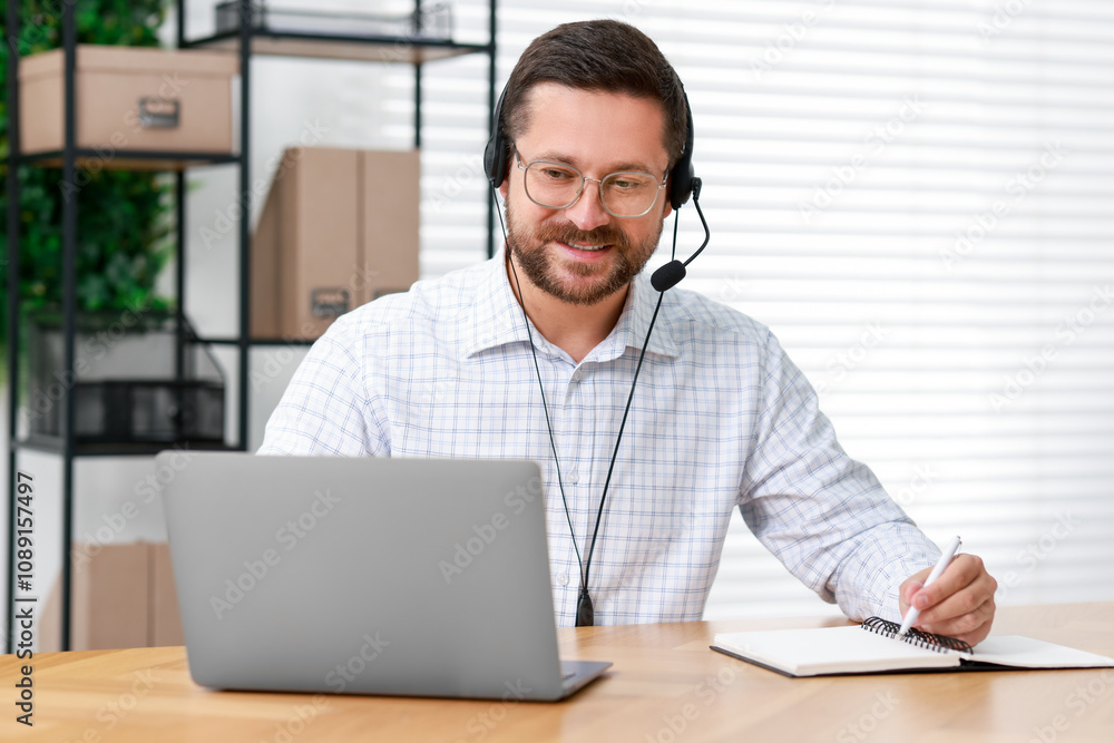 Interpreter in headset taking notes while having video chat via laptop at wooden table indoors Interpreter in headset taking notes while having video chat via laptop at wooden table indoors