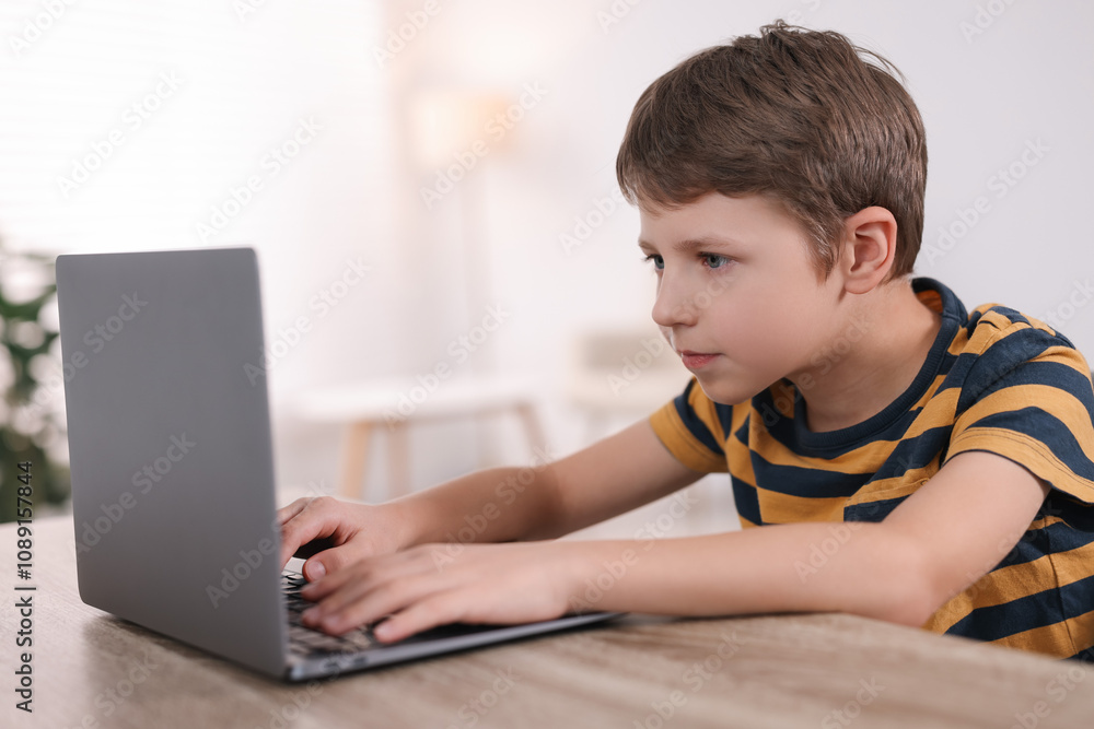 Boy with incorrect posture using laptop at wooden desk indoors Boy with incorrect posture using laptop at wooden desk indoors