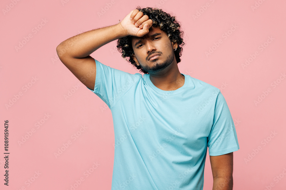 Young sad sick ill tired Indian man he wearing blue t-shirt casual clothes put hand on forehead suffer from headache isolated on plain pastel light pink background studio portrait. Lifestyle concept. Young sad sick ill tired Indian man he wearing blue t-shirt casual clothes put hand on forehead suffer from headache isolated on plain pastel light pink background studio portrait. Lifestyle concept.