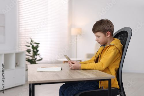 Boy with correct posture using smartphone at wooden desk indoors