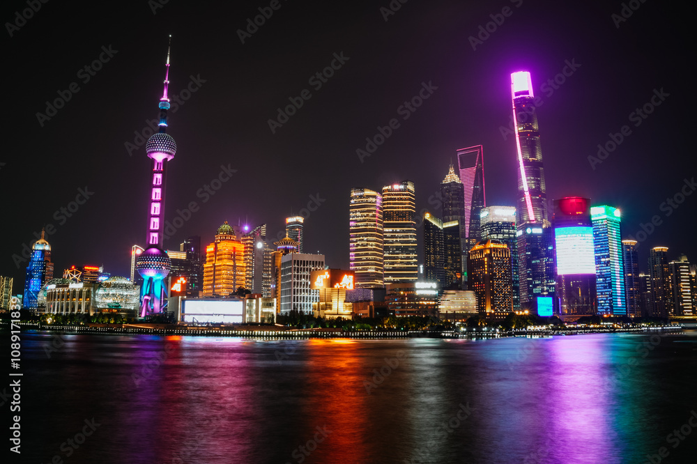 Fototapeta premium Night view of the illuminated skyline of Shanghai from the Bund, with the reflection of the lights in the river; Lujiazui, Shanghai, China