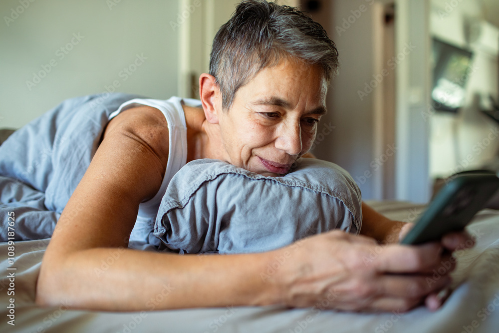 Senior woman using smartphone in bed after waking up in morning Senior woman using smartphone in bed after waking up in morning