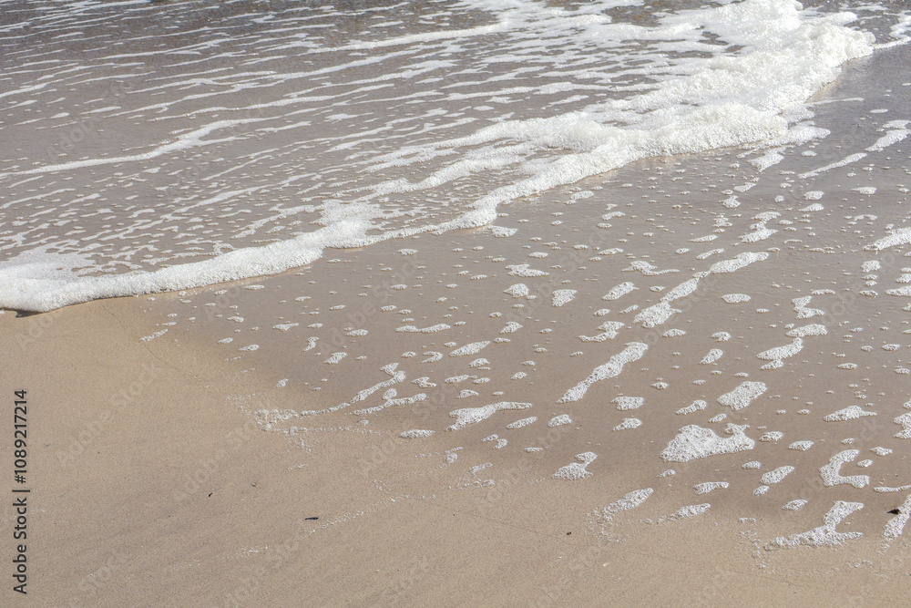 Close-up view of foamy sea waves softly washing over smooth sandy shore, showcasing natural textures and coastal serenity. Close-up view of foamy sea waves softly washing over smooth sandy shore, showcasing natural textures and coastal serenity.