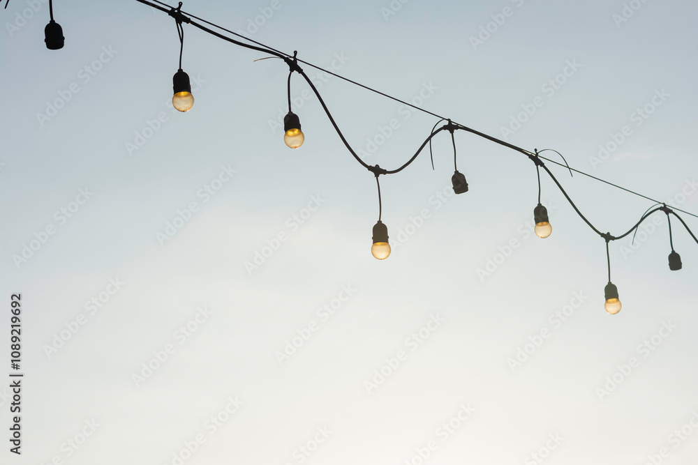 string of light bulbs hanging against a clear sky. The light bulbs are evenly spaced along the wire, which is slightly curved between the points where it is attached. string of light bulbs hanging against a clear sky. The light bulbs are evenly spaced along the wire, which is slightly curved between the points where it is attached.