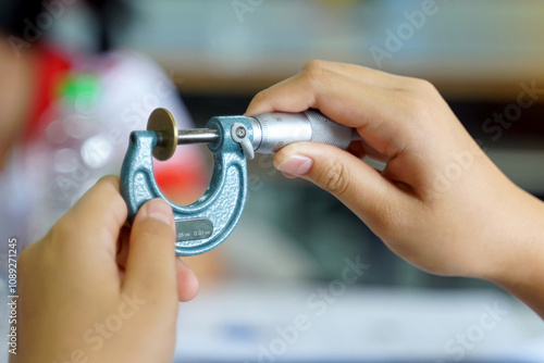 Thai student holds a micrometer to measure the thickness of a coin in millimetres. Concept of science laboratory, precision measuring instruments, measurement photo