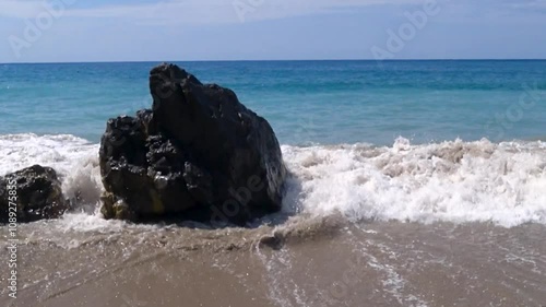 Huge rock on the foreshore with waves crashing on the seashore at sunset.
