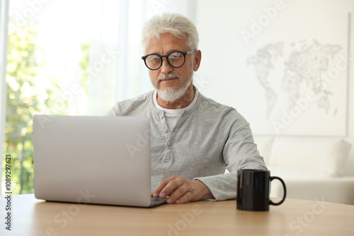 Senior man using laptop at table indoors