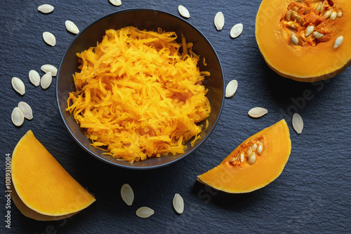 Konstfotografi Grated pumpkin in plate, parts of pumpkin and seeds on black table