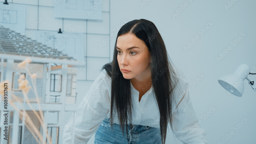 Young beautiful caucasian architect puts blueprint on the table and compare with house model while inspect hos model construction carefully at modern office with blueprint striped behind. Immaculate. Young beautiful caucasian architect puts blueprint on the table and compare with house model while inspect hos model construction carefully at modern office with blueprint striped behind. Immaculate.