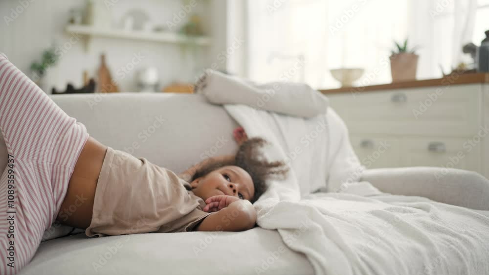 Funny little African girl lying on soft couch in living room, lazy weekend. Charming four-year-old child relaxing on sofa at home, comfortable and cozy apartment, carefree childhood, mixed race family Funny little African girl lying on soft couch in living room, lazy weekend. Charming four-year-old child relaxing on sofa at home, comfortable and cozy apartment, carefree childhood, mixed race family