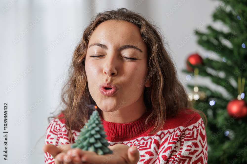 A happy young woman makes a wish by blowing out a candle in her hands in the shape of a Christmas tree. A happy young woman makes a wish by blowing out a candle in her hands in the shape of a Christmas tree.